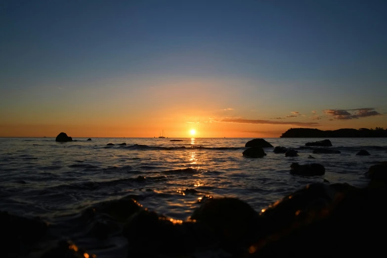 a sun rising above the ocean with a large rocky shore