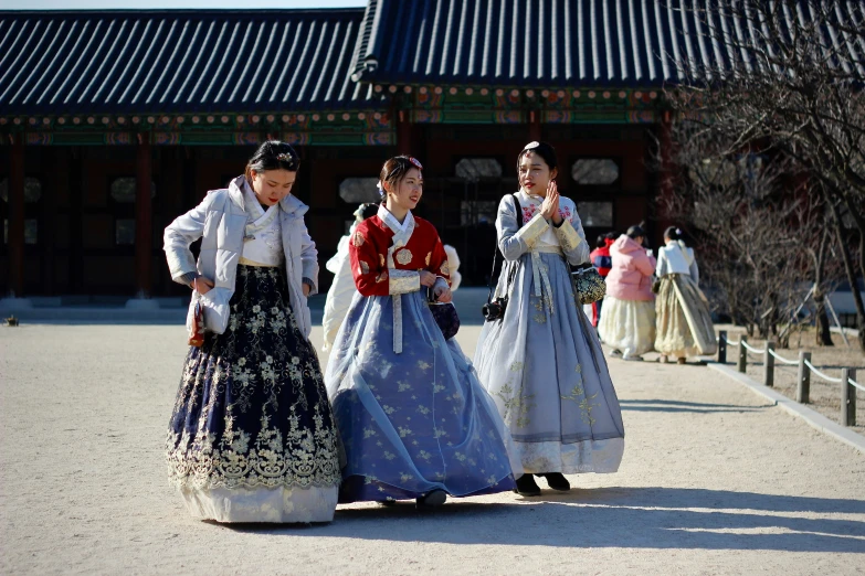 three women dressed in traditional clothing walking near a building