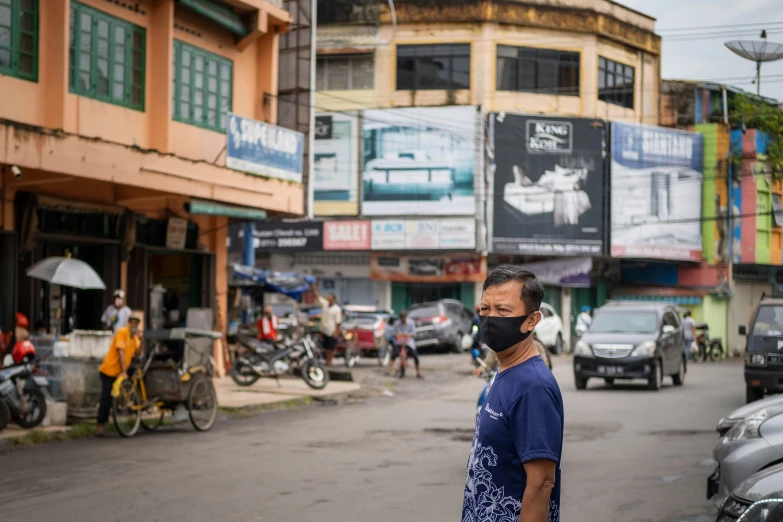 a man wearing a black face mask standing in front of some parked cars