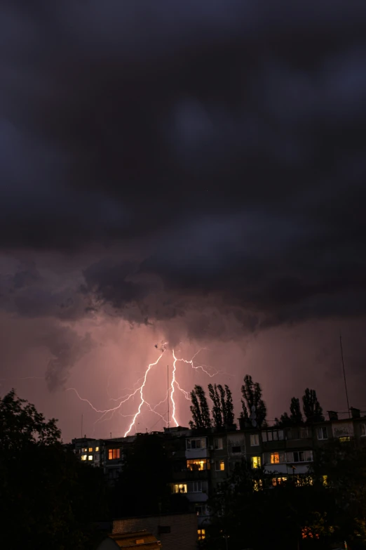 the lightning strikes above residential buildings on a cloudy night