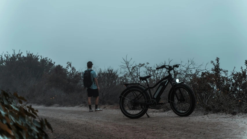 a man standing next to a bicycle on a dirt road