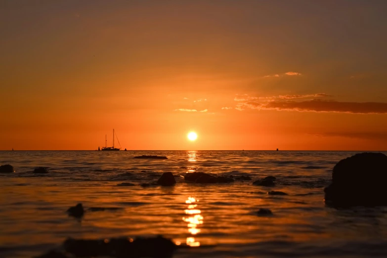 sunset in ocean with small rocks and large boat