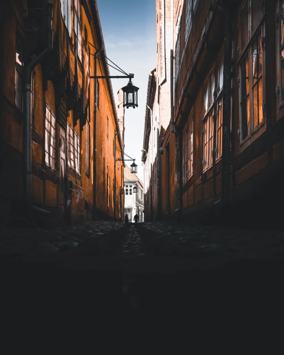 an alley with brick buildings and lamps hanging down