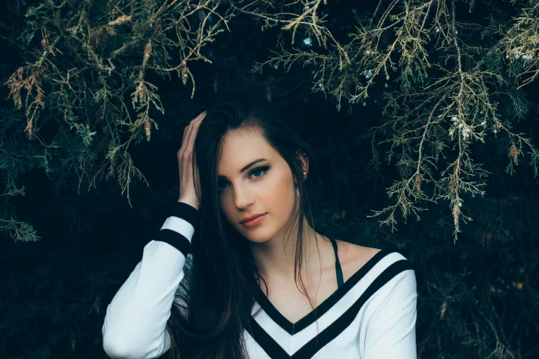 a woman poses in front of a tree and leaves