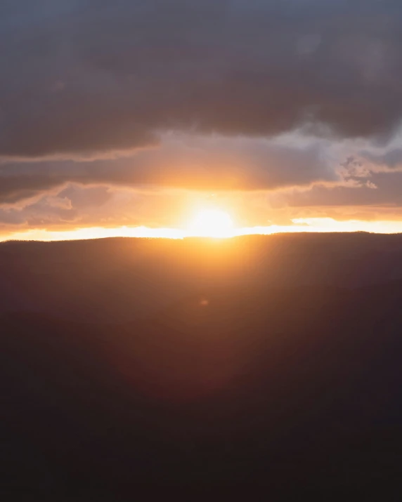 the sun is setting over a hill on a cloudy day