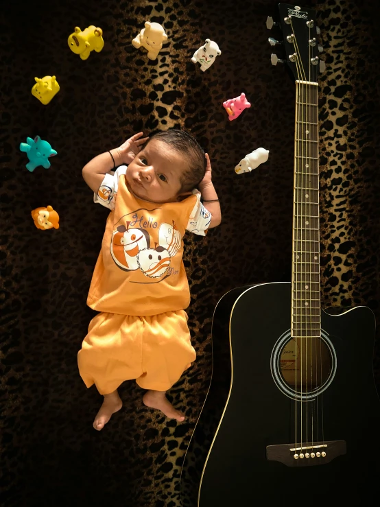 a small baby is laying on his stomach next to a guitar