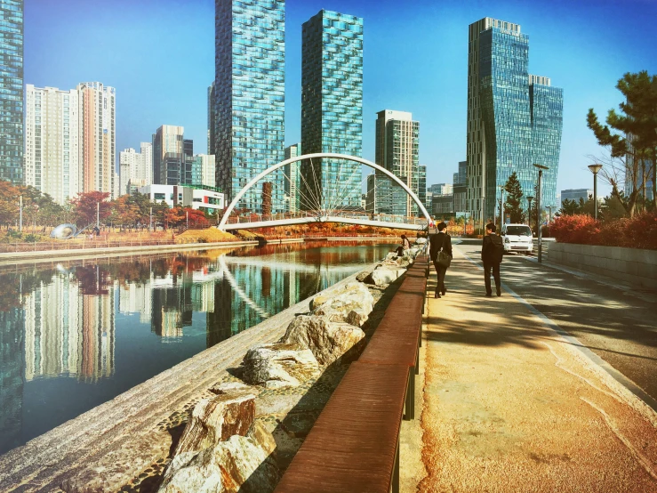 two people walking down a sidewalk next to some tall buildings