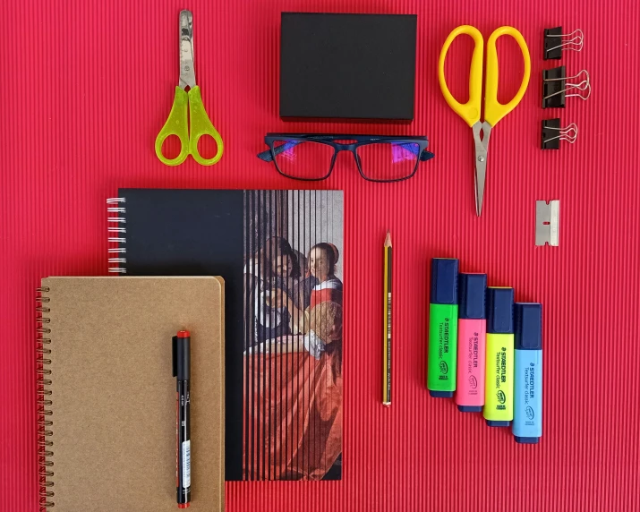 several school supplies on a red surface, including scissors, markers and pencils