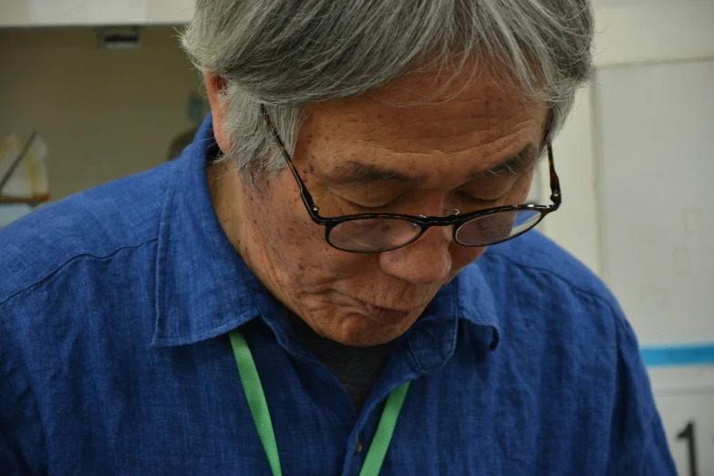 an elderly man wearing a blue shirt and glasses is looking down