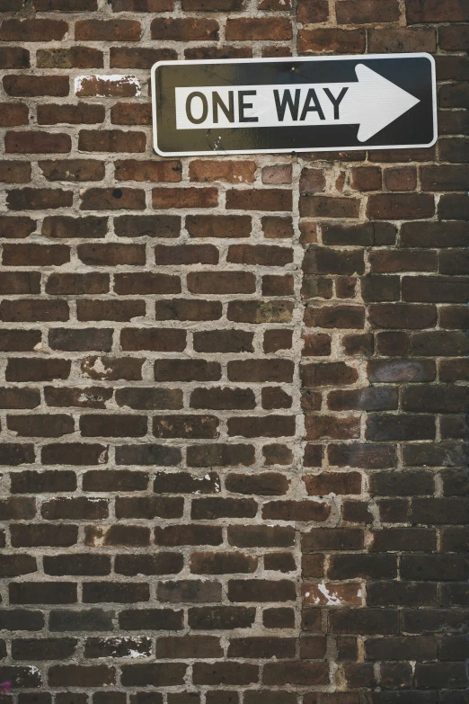 there is a one way sign mounted on the brick wall