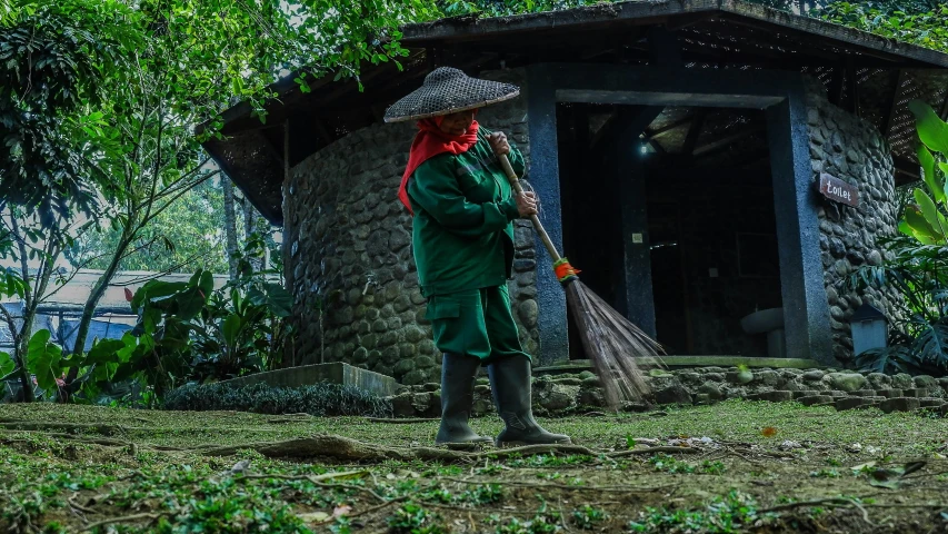 a woman standing outside of a mud hut with a broom in her hand