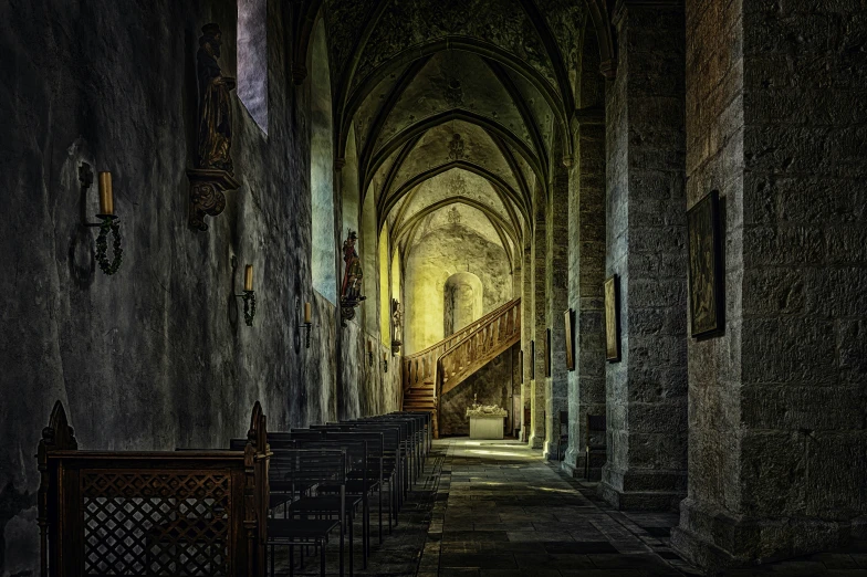 a gothic - styled staircase in a stone castle is lit by light from the window