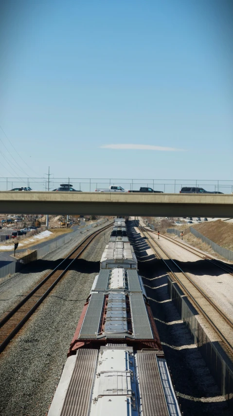 two trains traveling down tracks near a highway
