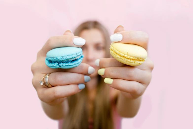 a girl holding out two macaroons that have been decorated with paste and jelly