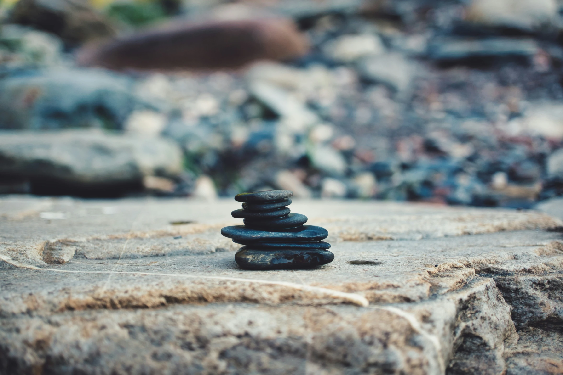 several stacked rocks sit atop some dirt near a rock beach