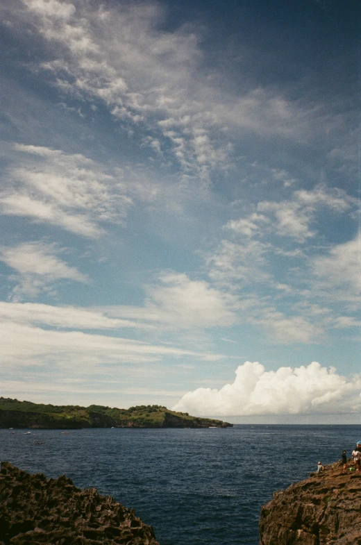 the lighthouse is at the end of the cliff with people sitting on it