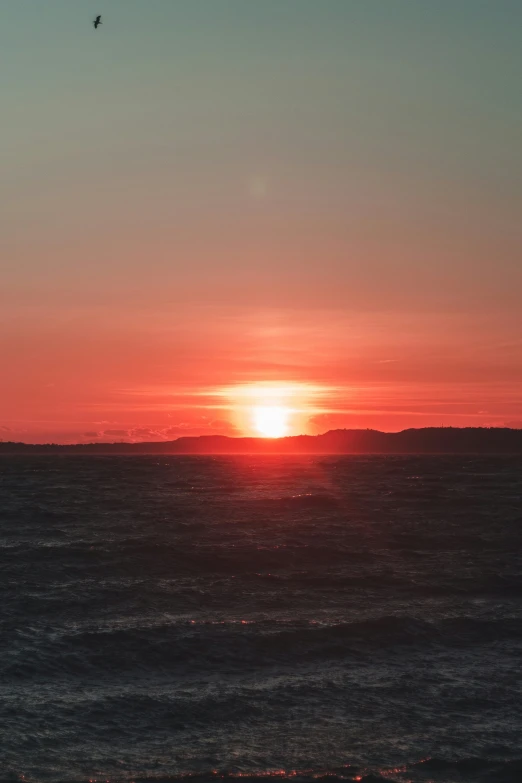 the sun set behind a distant mountain in the ocean