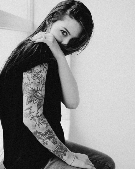 a woman sitting down posing with tattoos on her arms