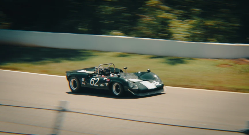 an old race car with two seats being driven on the track