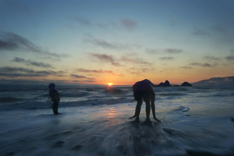 a person stands on the shore as the sun goes down