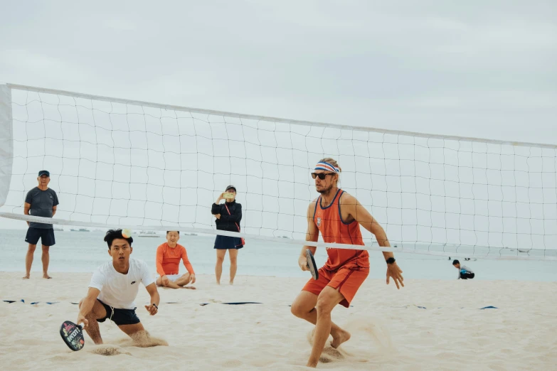 three men play volleyball on the beach with another man in red
