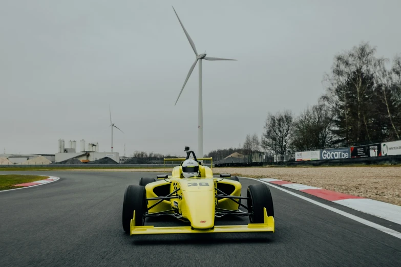 a yellow race car racing on a track with windmills