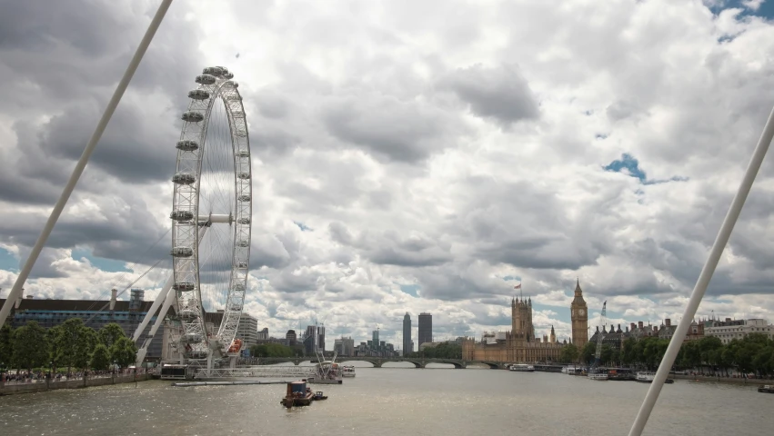 a ferris wheel on the river with clouds in the sky