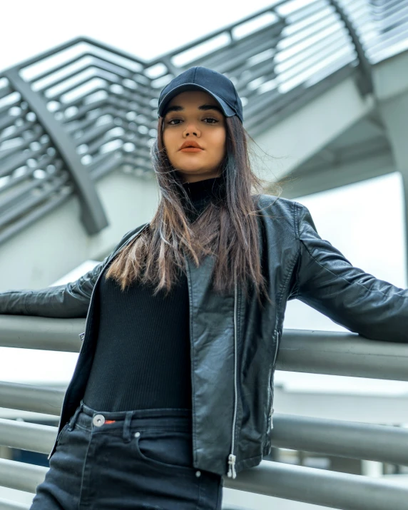 woman leaning against a railing wearing black outfit and hat