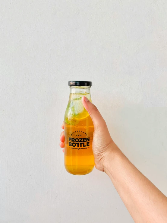 a woman holds a clear beer bottle in front of a plain wall