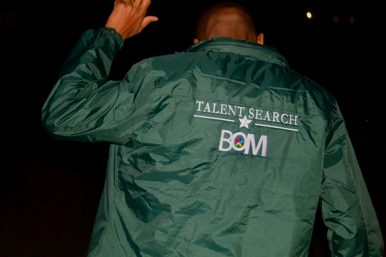 man in satin green jacket pointing up at his head