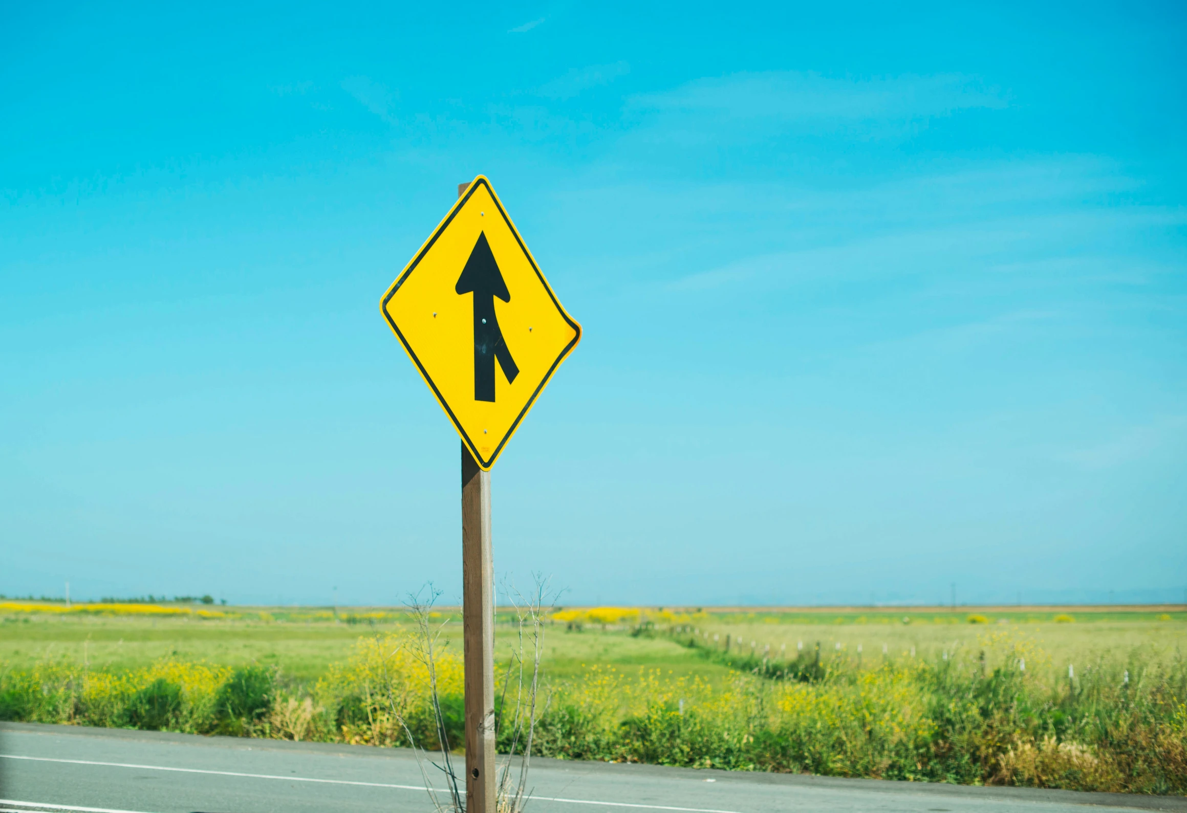 a yellow arrow sign on a wooden pole next to a road