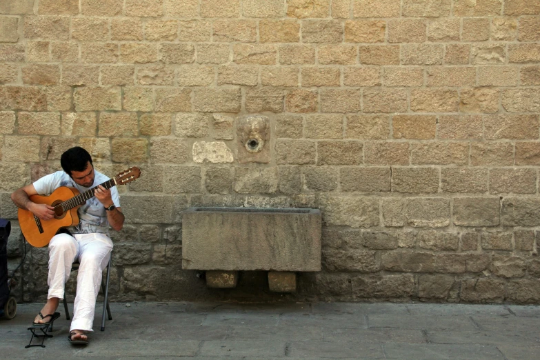 man playing guitar next to a wall with a small bench