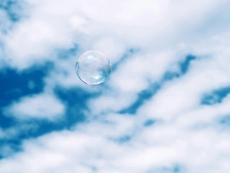 soap bubble floating across the air under a cloudy blue sky