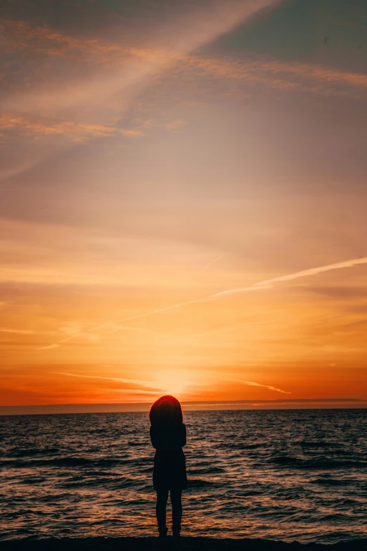 a person is standing on the shore at sunset