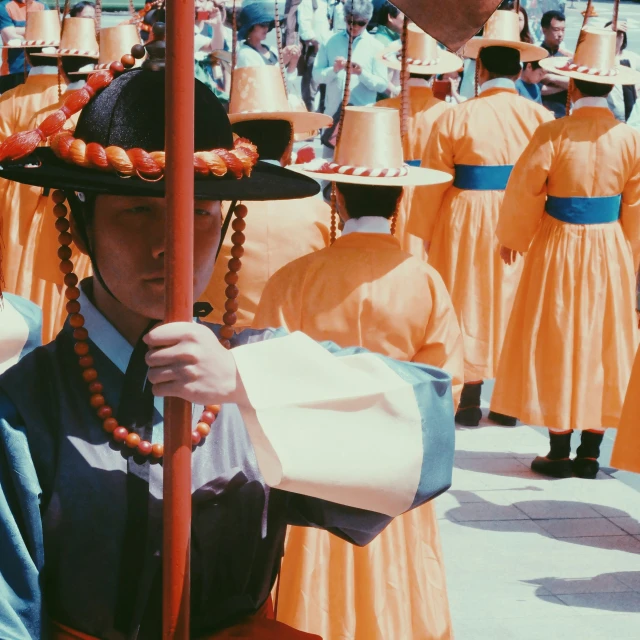 a young person with a large black hat on and orange clothing