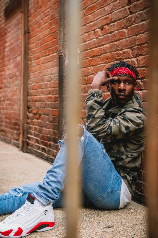 a man in blue jeans is leaning against a brick wall