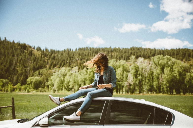 a woman sitting on the hood of a car in front of the woods