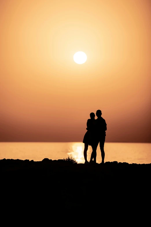 two people standing near the water at sunset