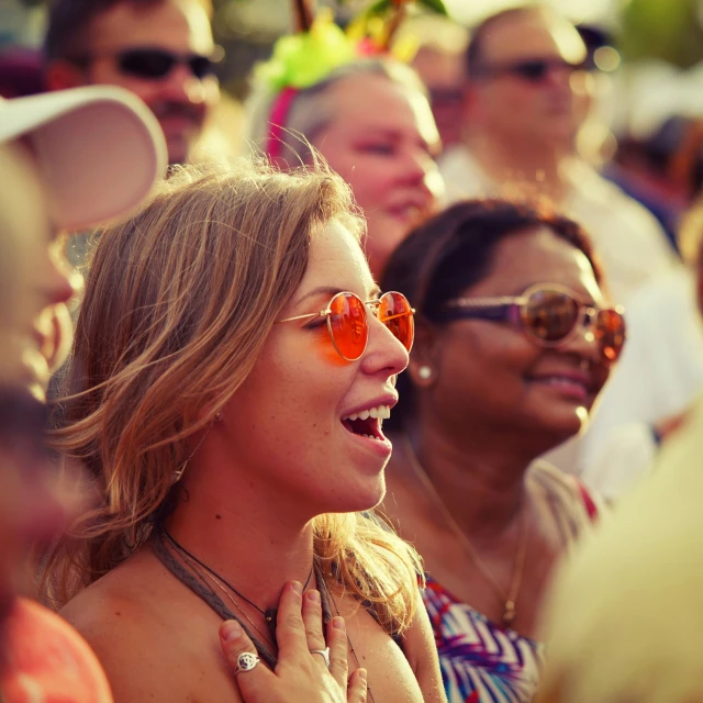 a woman in orange mirrored sunglasses stands among a crowd of people