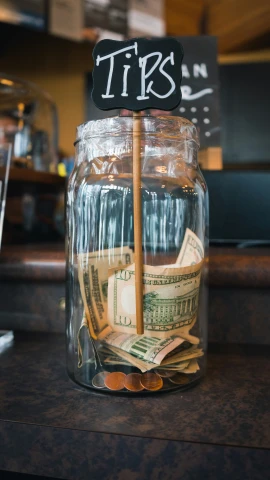a glass jar filled with money and tips sign