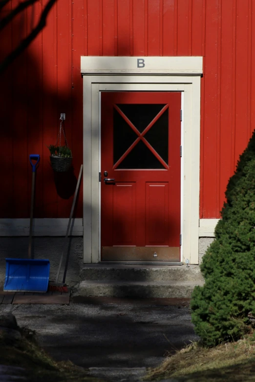 a bright red door with white trim stands out against the backdrop of a bright green bush and a blue shovel