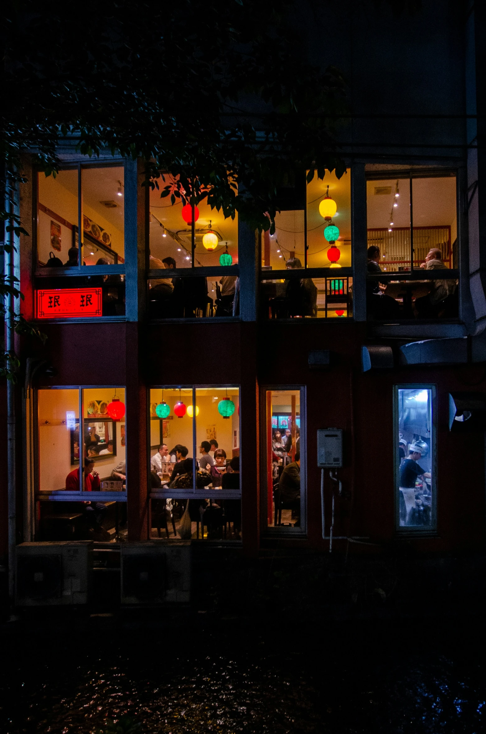 people at tables in the open front of a building with illuminated windows