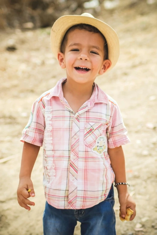 small boy in plaid shirt and hat walking in dirt field