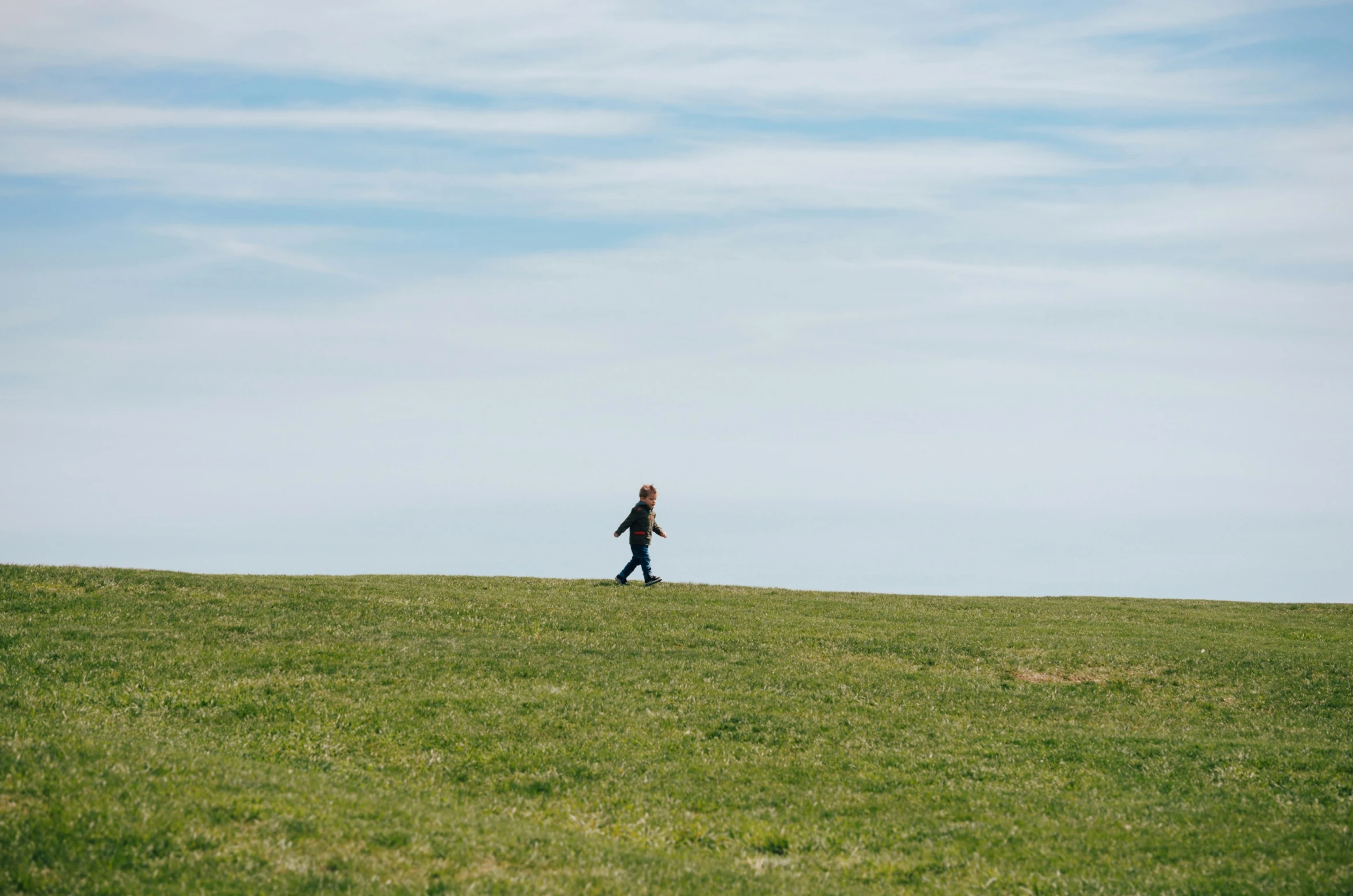 a woman walks along a green hill in a blue sky