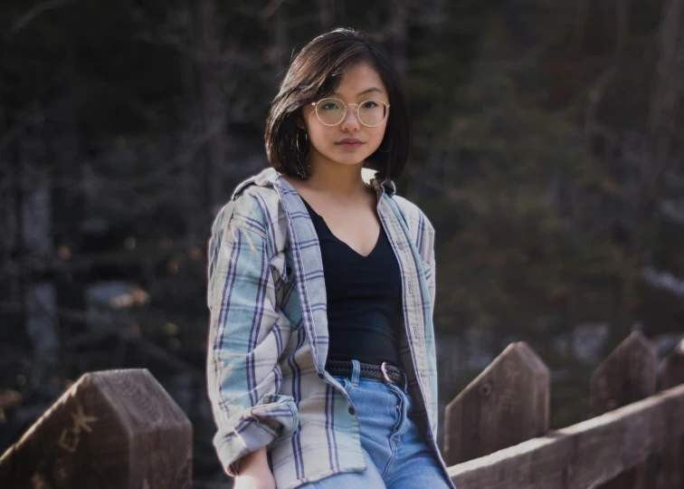 a girl poses on a wooden fence with a hand bag