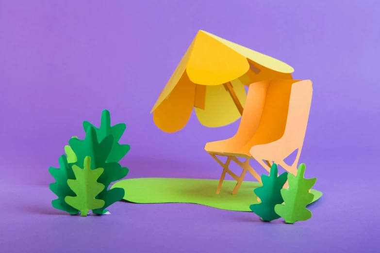 paper cut out of a yellow and orange chair with green tree on purple background