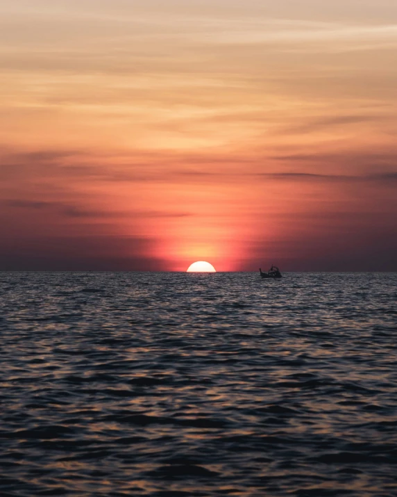 the sun setting over the ocean with a small boat in the water