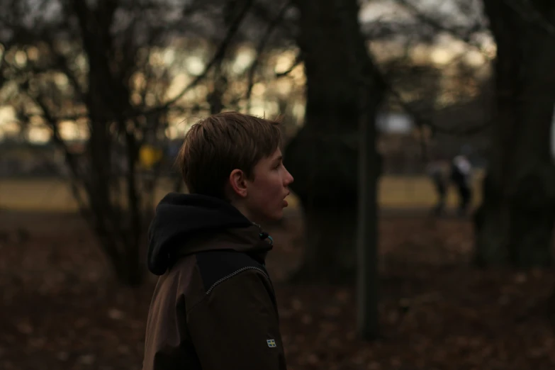 a young man standing near a leaf covered forest