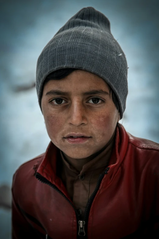 a portrait of an afghan child wearing a red leather jacket and a gray hat