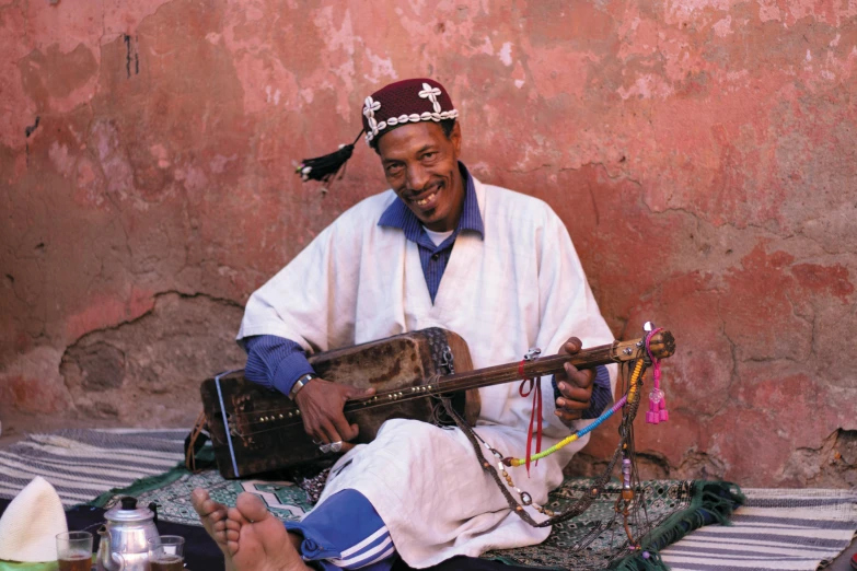 a man is sitting in front of a building holding an instrument